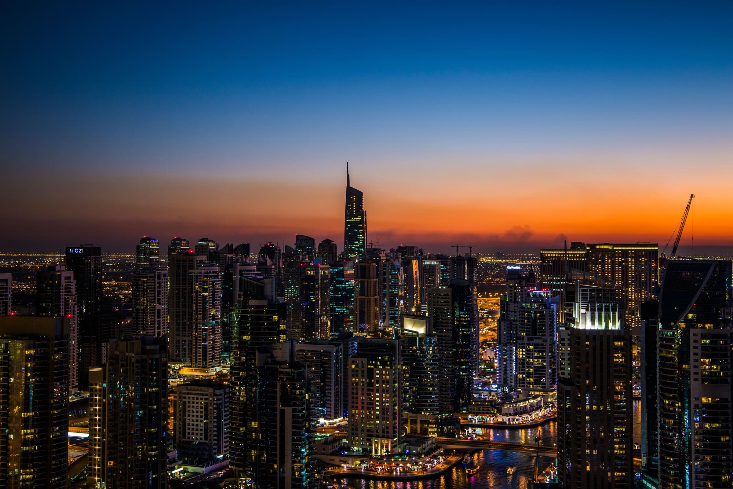 A city skyline at dusk, towers lit against an orange horizon